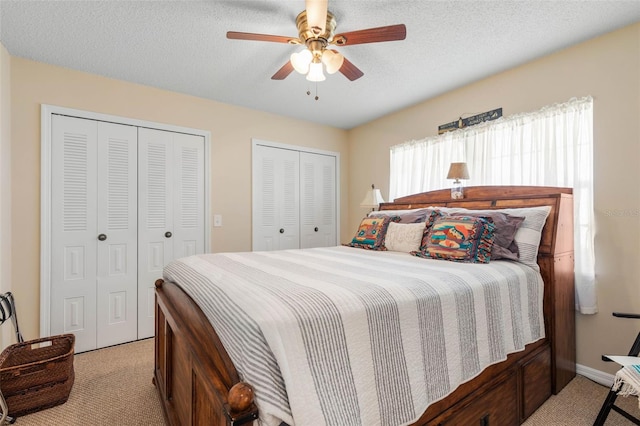 bedroom featuring a textured ceiling, ceiling fan, light colored carpet, and multiple closets