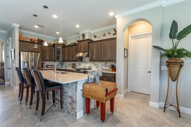 kitchen with backsplash, ornamental molding, dark brown cabinetry, light tile patterned floors, and a center island with sink