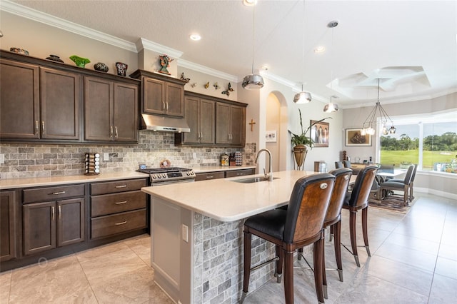 kitchen with light countertops, tasteful backsplash, under cabinet range hood, a sink, and a kitchen breakfast bar