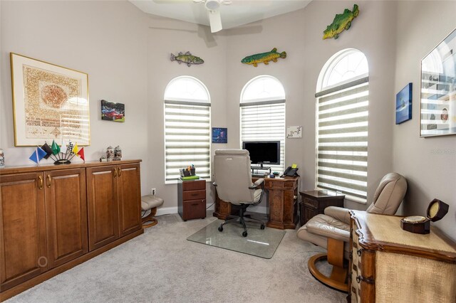 carpeted home office with ceiling fan and a towering ceiling