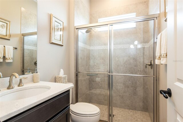 bathroom featuring a shower with door, vanity, and toilet