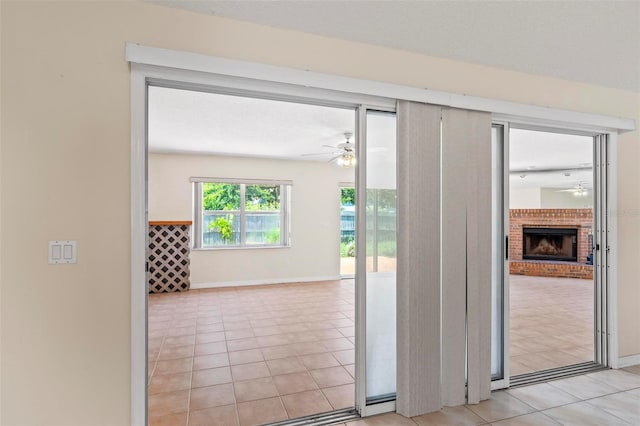 doorway to outside featuring ceiling fan, a brick fireplace, and light tile patterned flooring