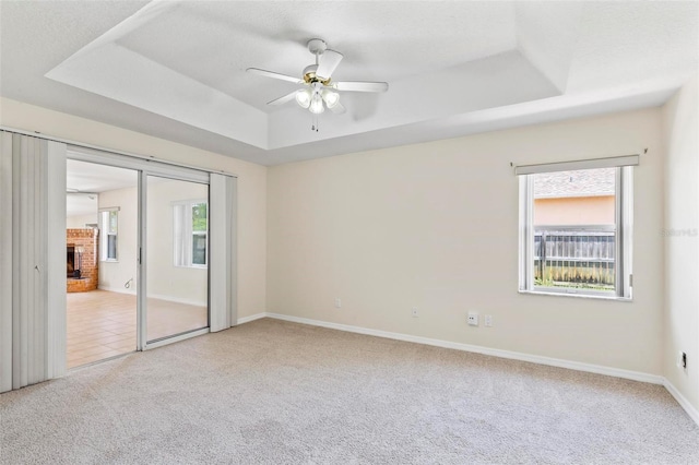 empty room featuring ceiling fan, a raised ceiling, a healthy amount of sunlight, and light carpet