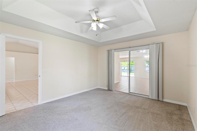 empty room featuring light colored carpet, a tray ceiling, and ceiling fan