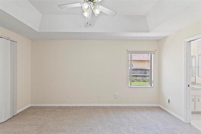 carpeted empty room featuring ceiling fan and a raised ceiling