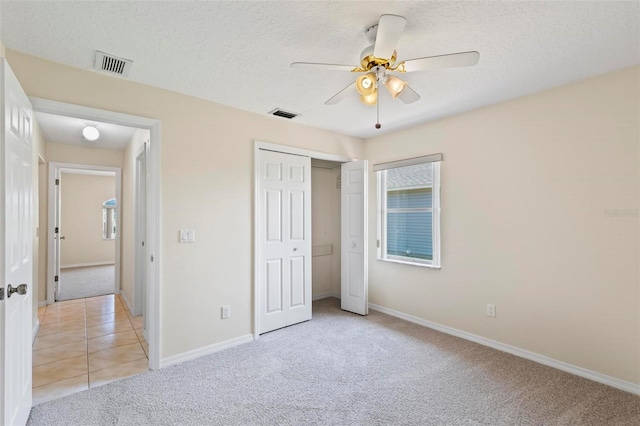 unfurnished bedroom featuring light colored carpet, a closet, a textured ceiling, and ceiling fan