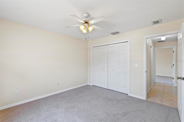 unfurnished bedroom featuring a textured ceiling, a closet, ceiling fan, and light carpet