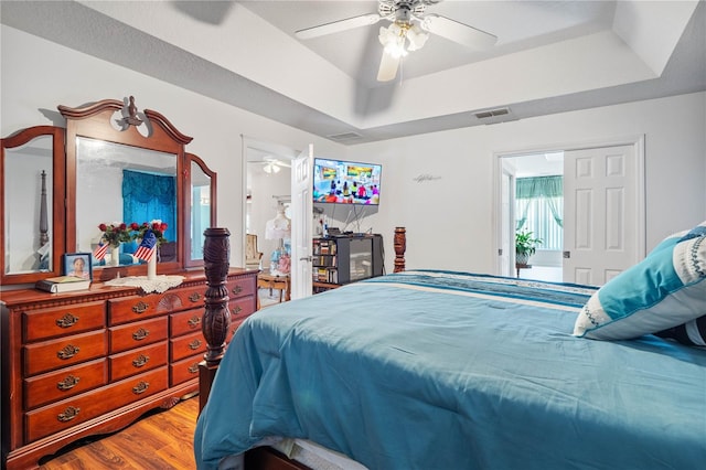 bedroom with light hardwood / wood-style floors, ceiling fan, and a raised ceiling