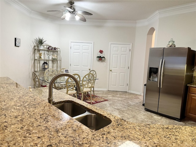 kitchen featuring ceiling fan, sink, light stone countertops, crown molding, and stainless steel fridge