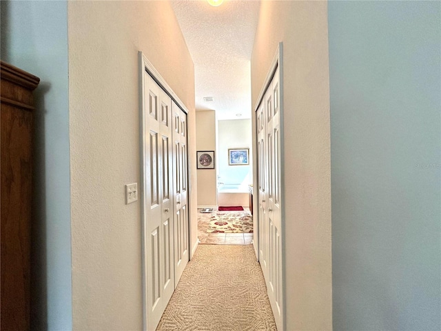 hallway featuring a textured ceiling and light carpet