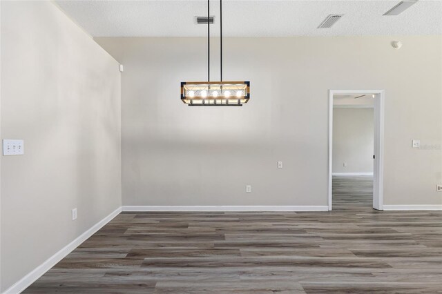 unfurnished dining area featuring wood-type flooring, a notable chandelier, and a textured ceiling