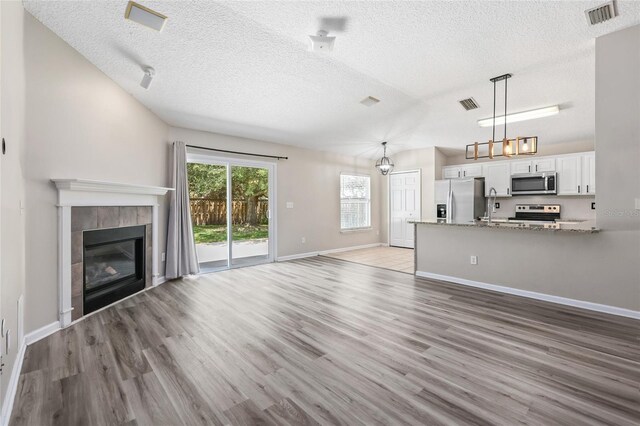 unfurnished living room with light hardwood / wood-style floors, sink, a tile fireplace, and a textured ceiling