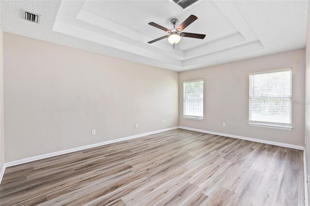 unfurnished room with a tray ceiling, light hardwood / wood-style flooring, ceiling fan, and a textured ceiling