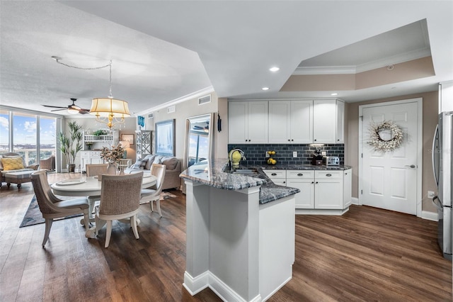 kitchen featuring sink, crown molding, a raised ceiling, kitchen peninsula, and dark wood-type flooring