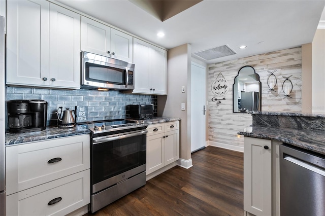 kitchen featuring appliances with stainless steel finishes, decorative backsplash, white cabinets, dark stone counters, and dark wood-type flooring