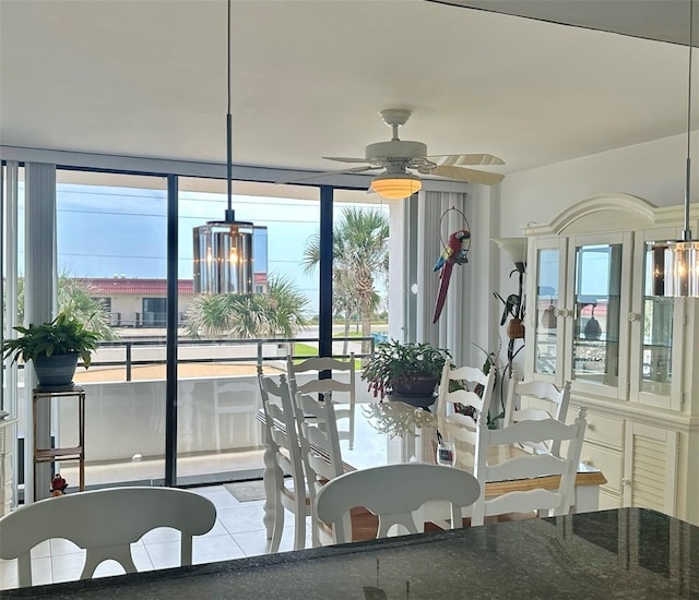 dining space with light tile patterned floors, a wall of windows, ceiling fan with notable chandelier, and a healthy amount of sunlight