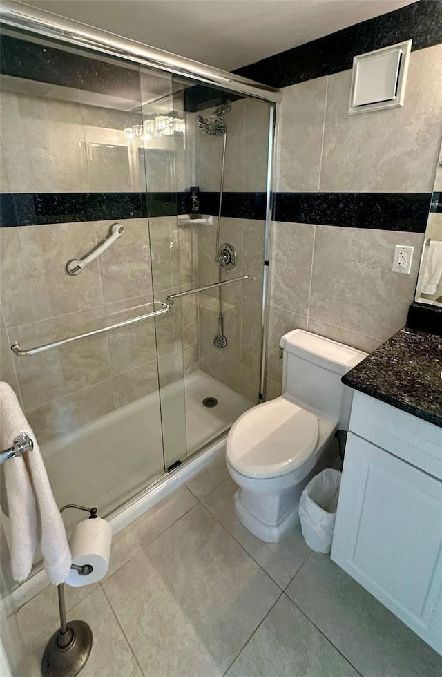 bathroom featuring tile patterned flooring, toilet, vanity, tile walls, and a shower stall