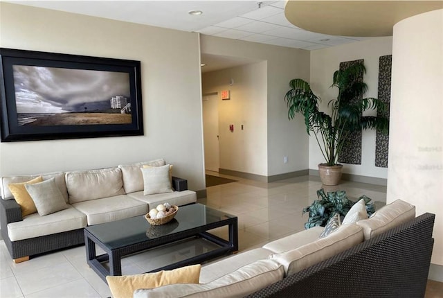 living room featuring a paneled ceiling, light tile patterned floors, and baseboards