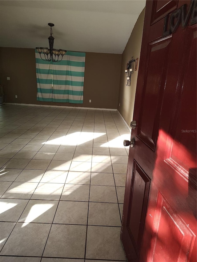 empty room with light tile patterned flooring, vaulted ceiling, and a notable chandelier