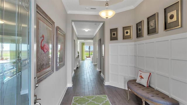 hallway with a raised ceiling, crown molding, and dark wood-type flooring