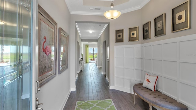 hallway with dark wood-style floors, baseboards, a decorative wall, and crown molding