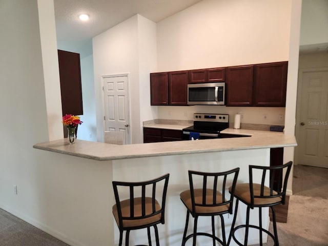 kitchen with a kitchen bar, light carpet, stainless steel appliances, and kitchen peninsula