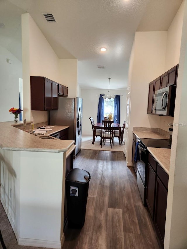 kitchen with kitchen peninsula, dark brown cabinets, dark hardwood / wood-style flooring, stainless steel appliances, and decorative light fixtures