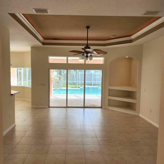 empty room with built in shelves, ceiling fan, light tile patterned flooring, and a tray ceiling