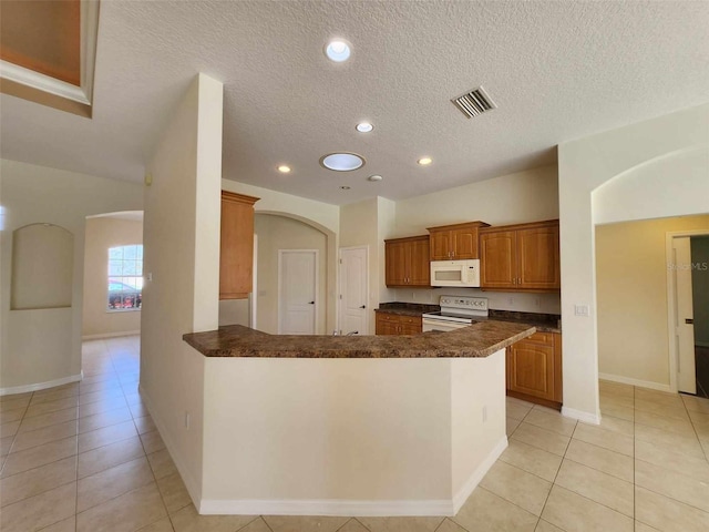 kitchen featuring a textured ceiling, kitchen peninsula, light tile patterned floors, and white appliances