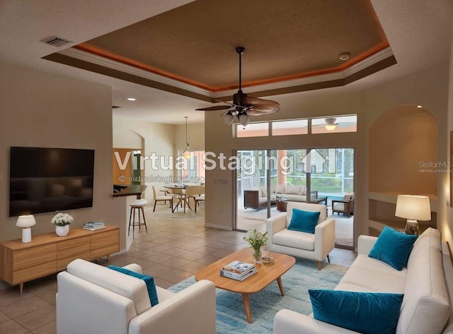 tiled living room with a tray ceiling, ceiling fan, and ornamental molding