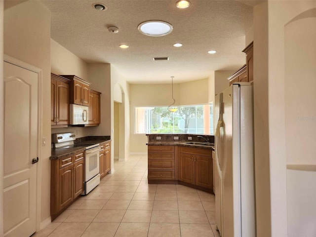 kitchen with a textured ceiling, white appliances, sink, decorative light fixtures, and light tile patterned flooring