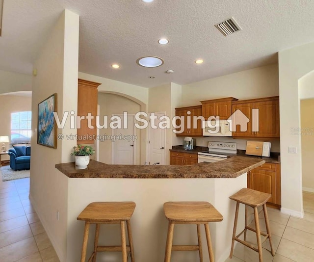 kitchen featuring kitchen peninsula, a kitchen breakfast bar, white appliances, a textured ceiling, and light tile patterned flooring