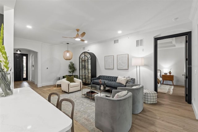 living area with light wood-type flooring, visible vents, arched walkways, and crown molding