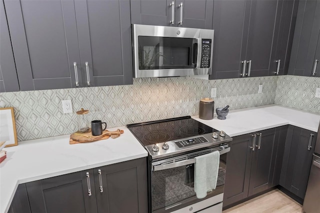 kitchen with light hardwood / wood-style floors, light stone counters, appliances with stainless steel finishes, and decorative backsplash