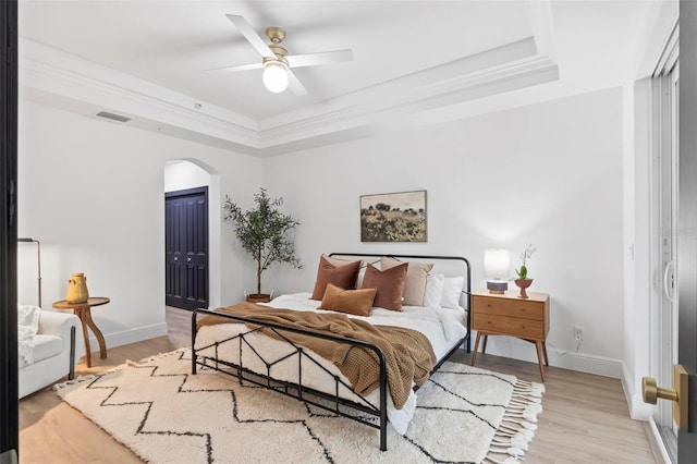 bedroom featuring visible vents, light wood finished floors, baseboards, arched walkways, and a raised ceiling