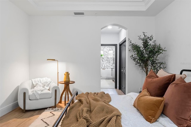 bedroom featuring a tray ceiling, connected bathroom, crown molding, and light hardwood / wood-style flooring