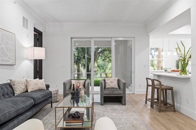 living area with visible vents, baseboards, light wood-style floors, and ornamental molding