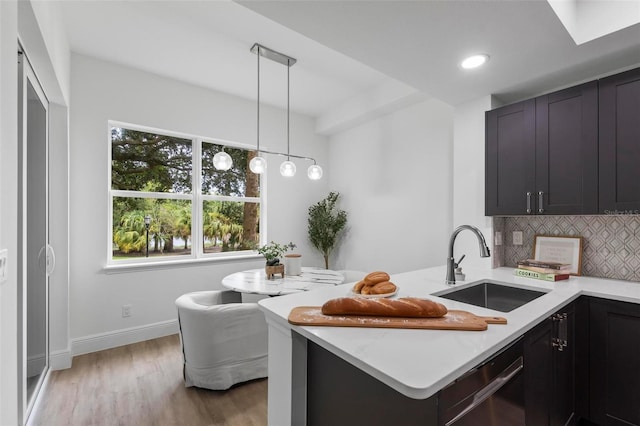 kitchen featuring backsplash, dishwasher, light wood-type flooring, a peninsula, and a sink