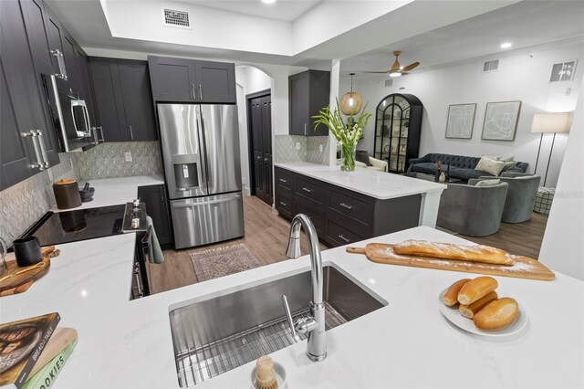 kitchen featuring visible vents, a peninsula, light wood-style flooring, arched walkways, and appliances with stainless steel finishes