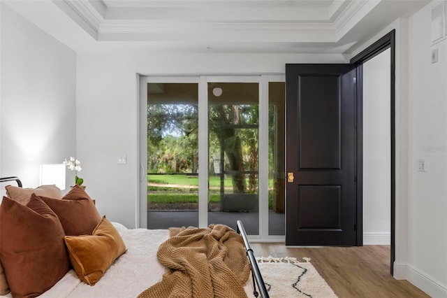 bedroom featuring light wood finished floors, a raised ceiling, crown molding, and access to outside