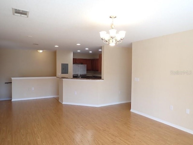 unfurnished living room with electric panel, hardwood / wood-style floors, and an inviting chandelier