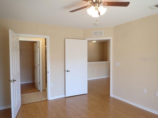 unfurnished bedroom featuring a spacious closet, a closet, ceiling fan, and wood-type flooring