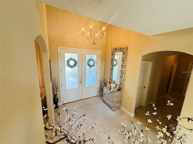 foyer with arched walkways, a chandelier, baseboards, vaulted ceiling, and french doors