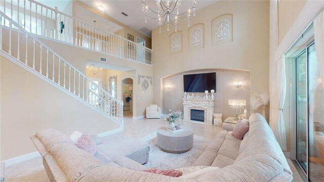 living room with plenty of natural light, a notable chandelier, a high end fireplace, and a towering ceiling