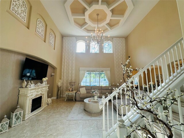 tiled living room featuring coffered ceiling, a high ceiling, a premium fireplace, and an inviting chandelier