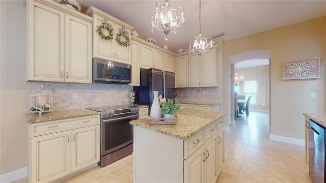 kitchen with arched walkways, light stone counters, appliances with stainless steel finishes, cream cabinetry, and a chandelier