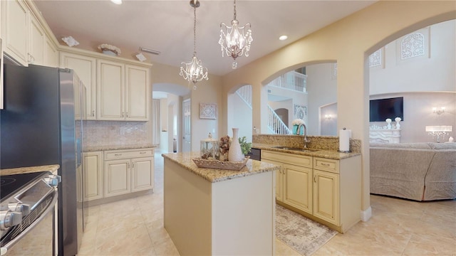 kitchen featuring arched walkways, a kitchen island, stove, cream cabinets, and a sink