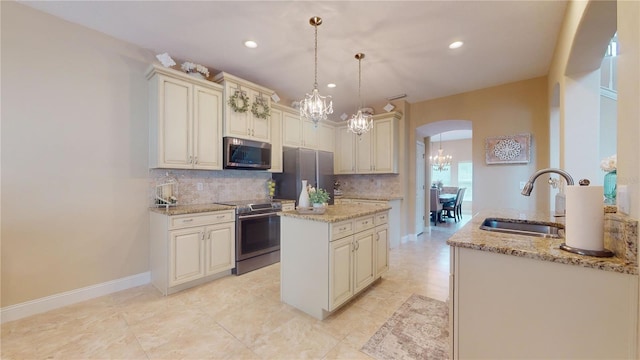 kitchen with arched walkways, cream cabinets, a sink, appliances with stainless steel finishes, and decorative backsplash