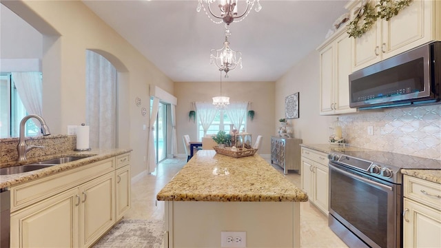 kitchen with a kitchen island, stainless steel appliances, cream cabinetry, a chandelier, and a sink