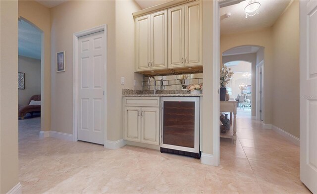 kitchen featuring backsplash, beverage cooler, cream cabinets, light stone countertops, and light tile patterned floors